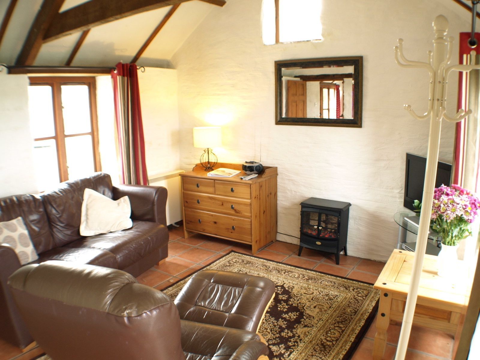 A cozy living room with a brown leather sofa, a wooden dresser, a rug, and a television.