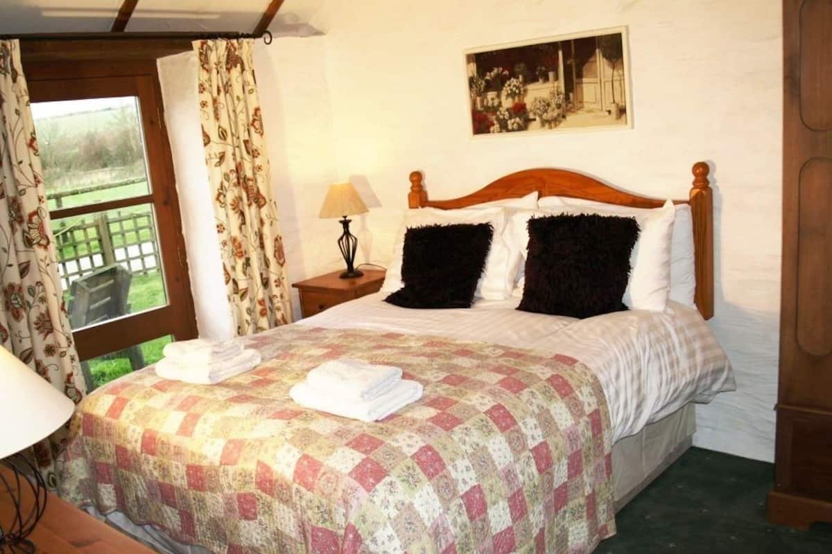 A neatly made bed with a floral quilt, a wooden headboard, and a painting on the wall.