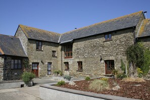 A stone building with multiple windows and doors, a courtyard with plants, and a clear blue sky. - Polean Farm Cottages (Looe)
