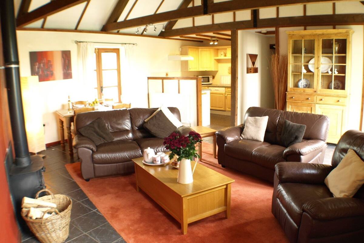 A cozy living room with leather sofas, a wooden coffee table, and a kitchen in the background.