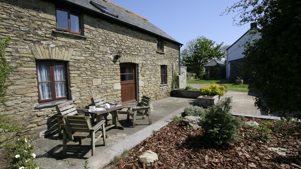 A stone building with a patio area featuring a table and chairs, surrounded by a garden with mulch and plants.