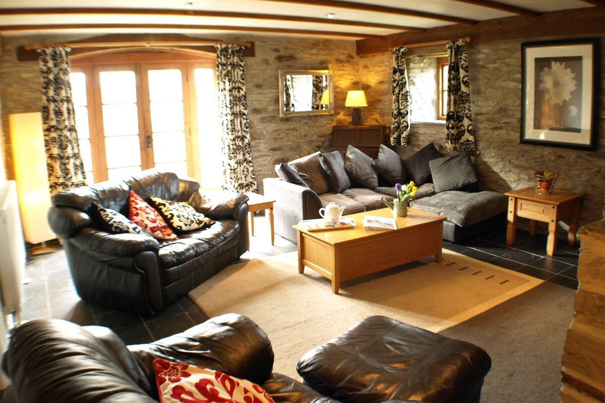 A cozy living room with leather sofas, a wooden coffee table, and a stone wall.