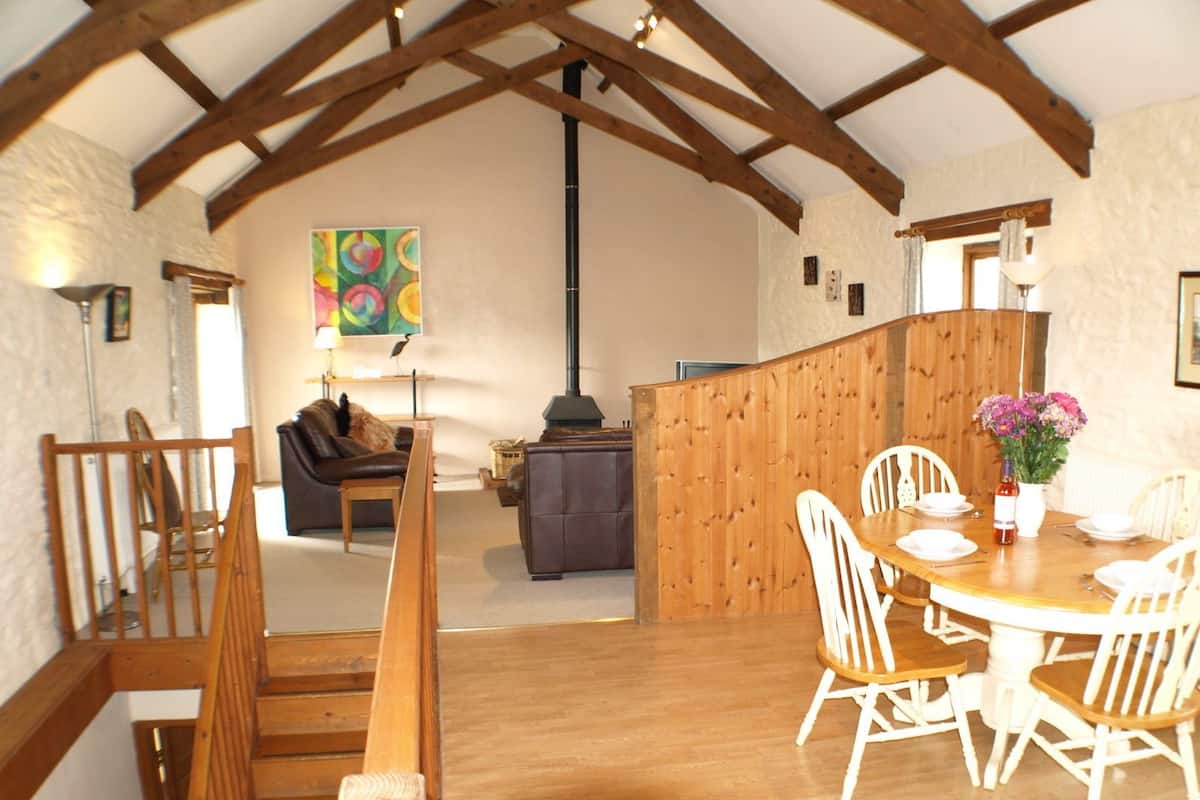 A cozy interior with a wooden dining table, white chairs, a sofa, and a colorful abstract painting on the wall.