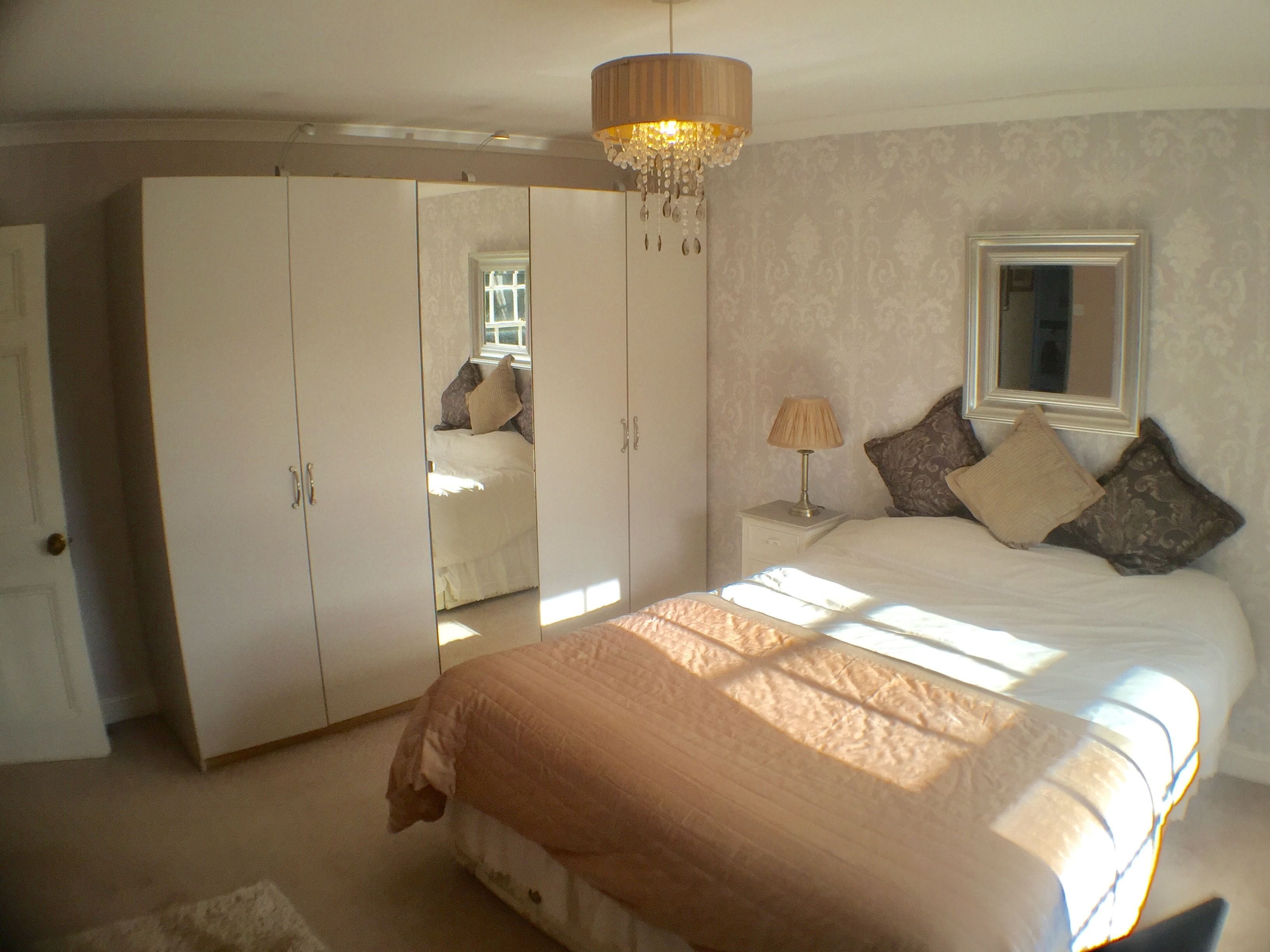 A bedroom with a bed, a wardrobe, a nightstand, a lamp, and a window.
