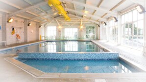 An indoor swimming pool with clear glass walls, a tiled blue edge, and overhead lighting.