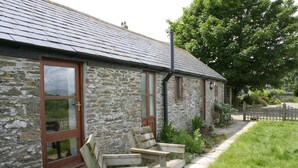 A stone building with a tiled roof, wooden benches, and a paved pathway. - Polean Farm Cottages (Looe)