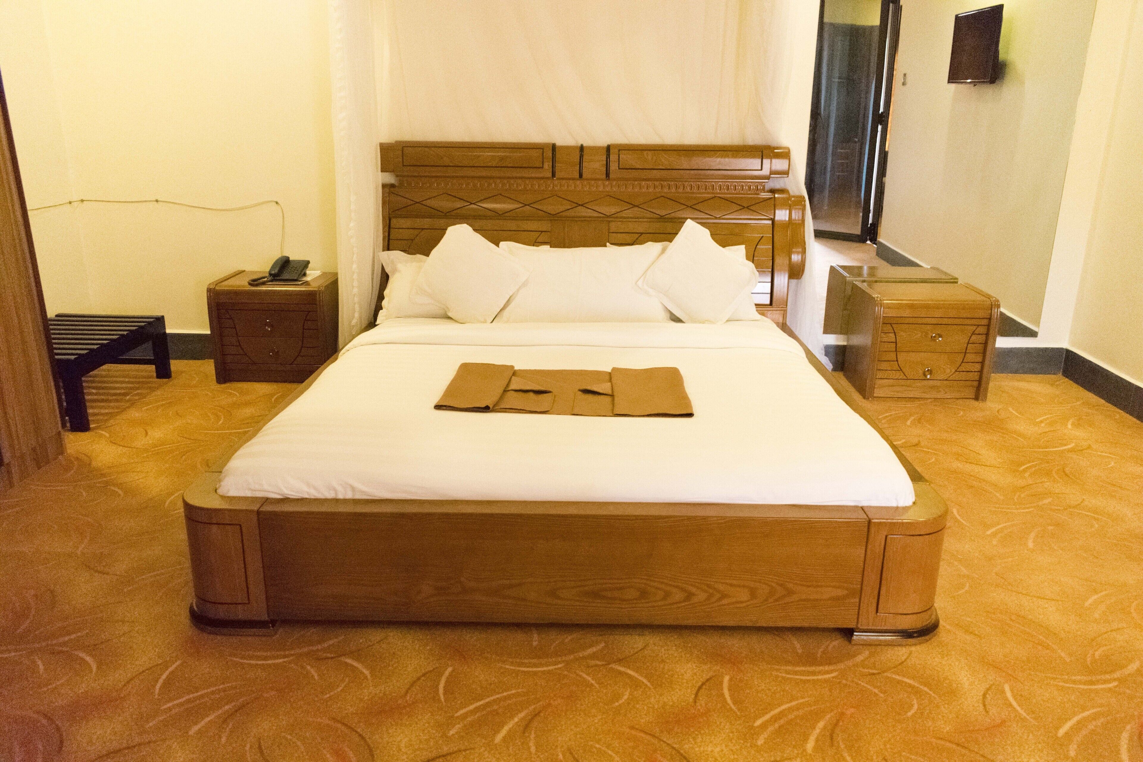 Een net opgemaakt bed met een houten hoofdbord, een nachtkastje met een telefoon, en een klein nachtkastje.