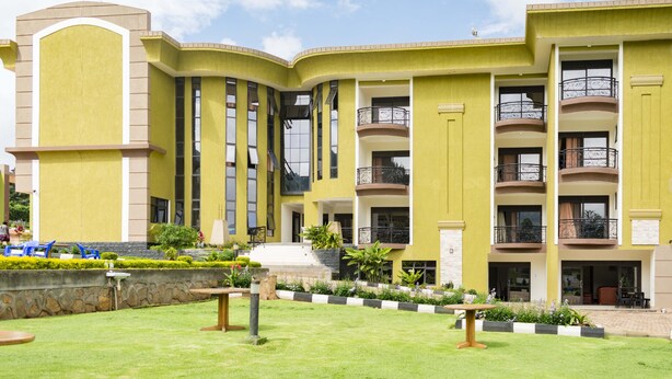 Un hotel de varios pisos con fachada amarilla, balcones y un patio ajardinado con zonas de estar.