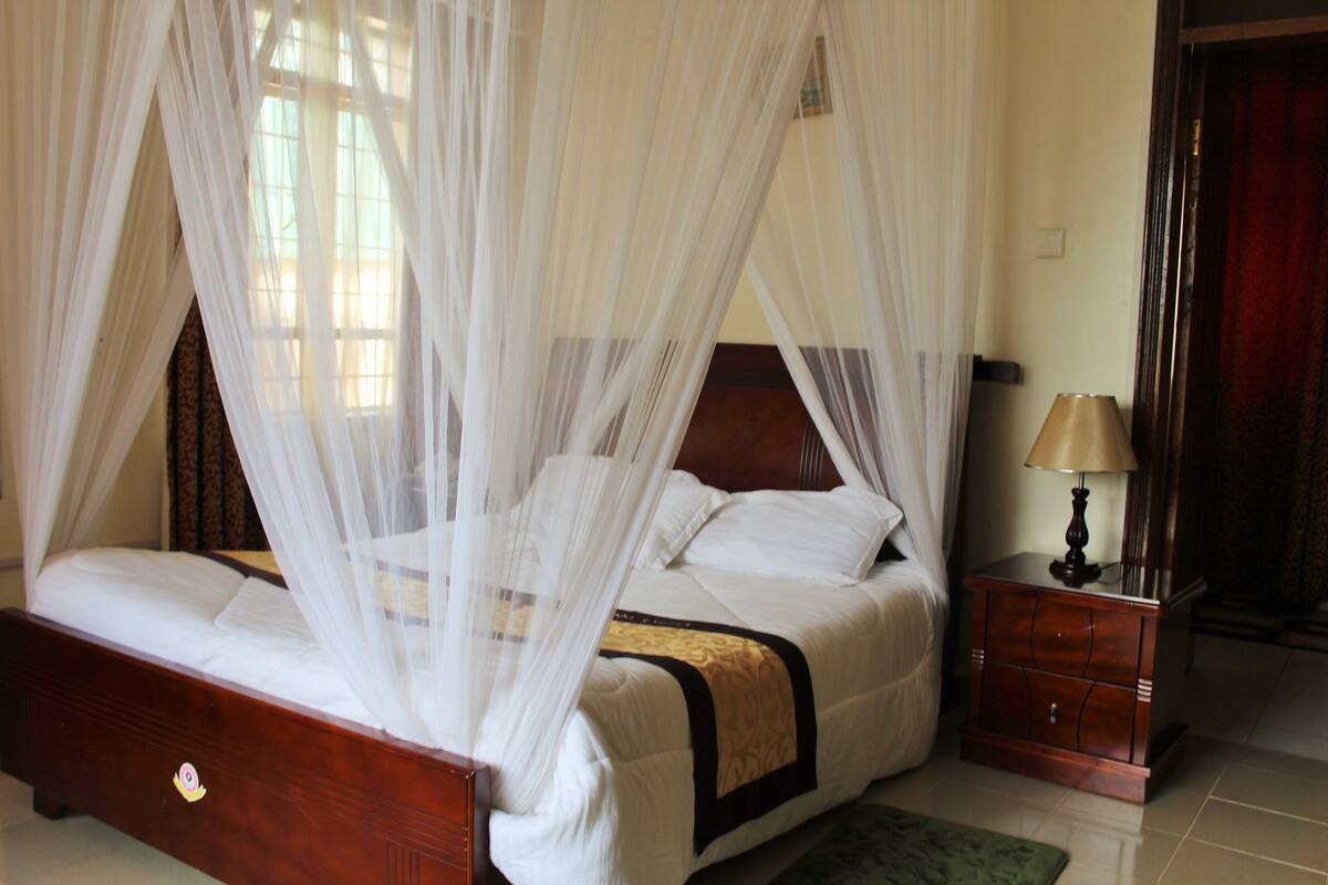 A four-poster bed with a canopy, a bedside table with a lamp, and a green rug.