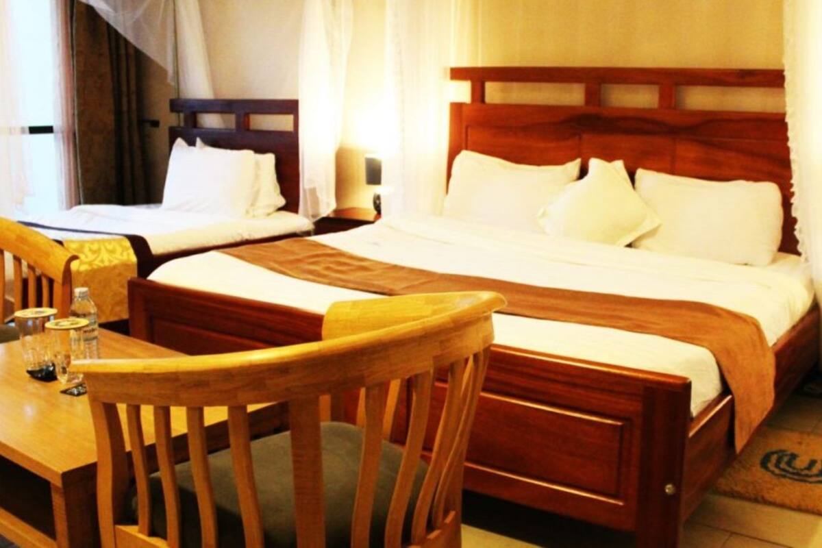 A hotel room with two beds, wooden furniture, a small table, and a bedside table with a lamp.