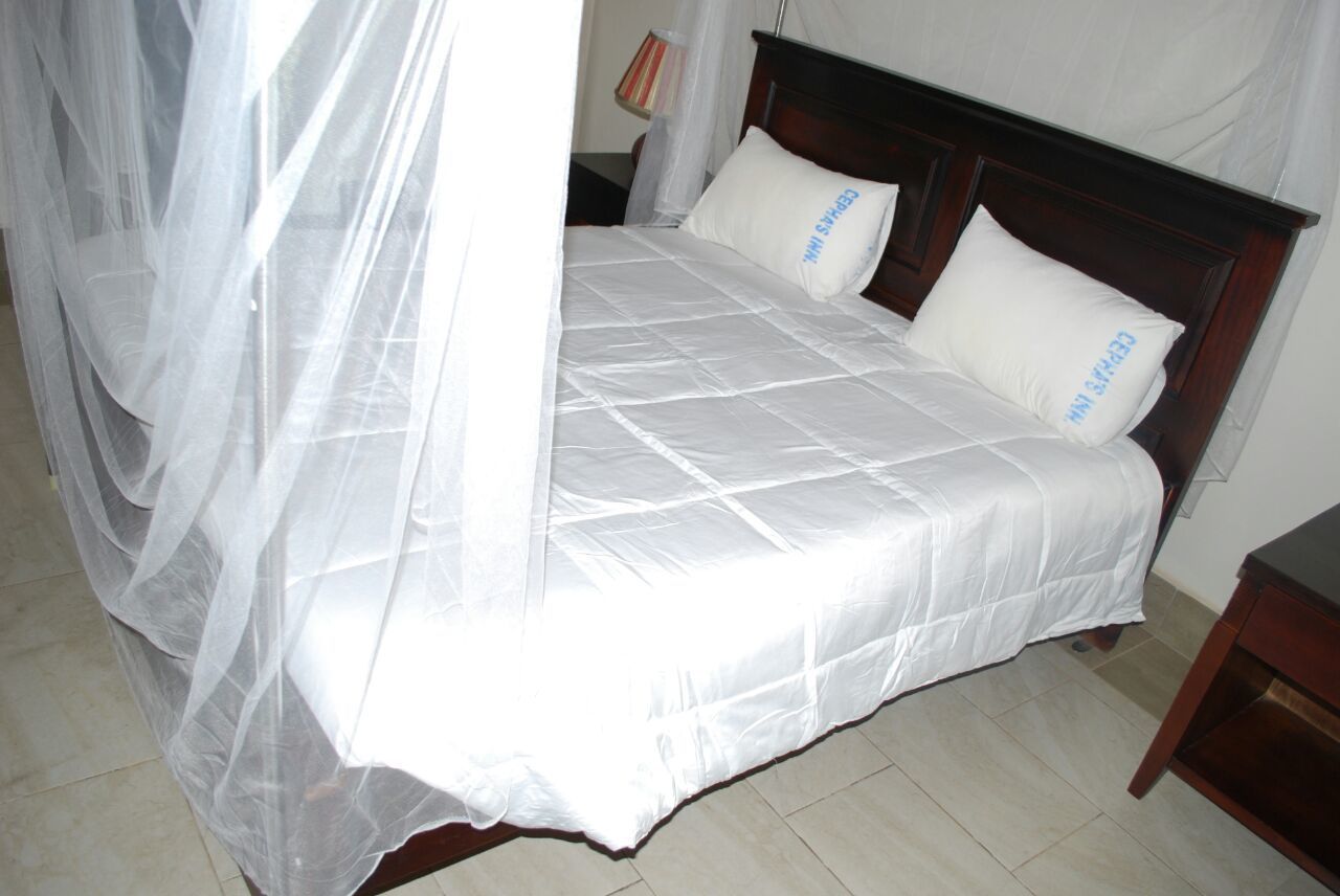 Un letto con copriletto bianco e due cuscini, una testiera in legno e un comodino con una lampada.