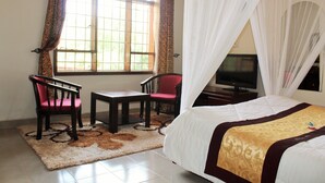 Habitación de hotel con cama, televisión, escritorio, dos sillas y ventana con cortinas.