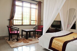 A hotel room with a bed, a television, a desk, two chairs, and a window with curtains.