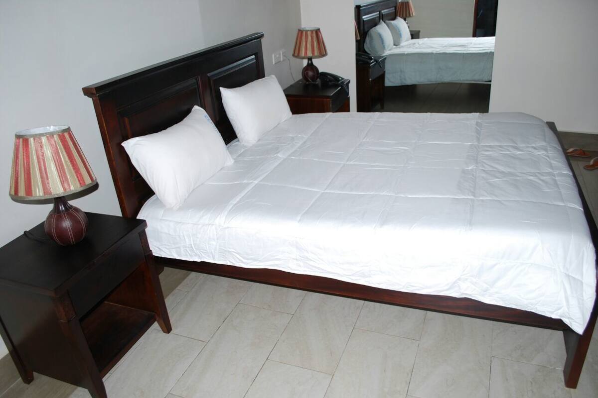 A neatly made bed with white bedding, a wooden headboard, and a bedside lamp on a matching nightstand.