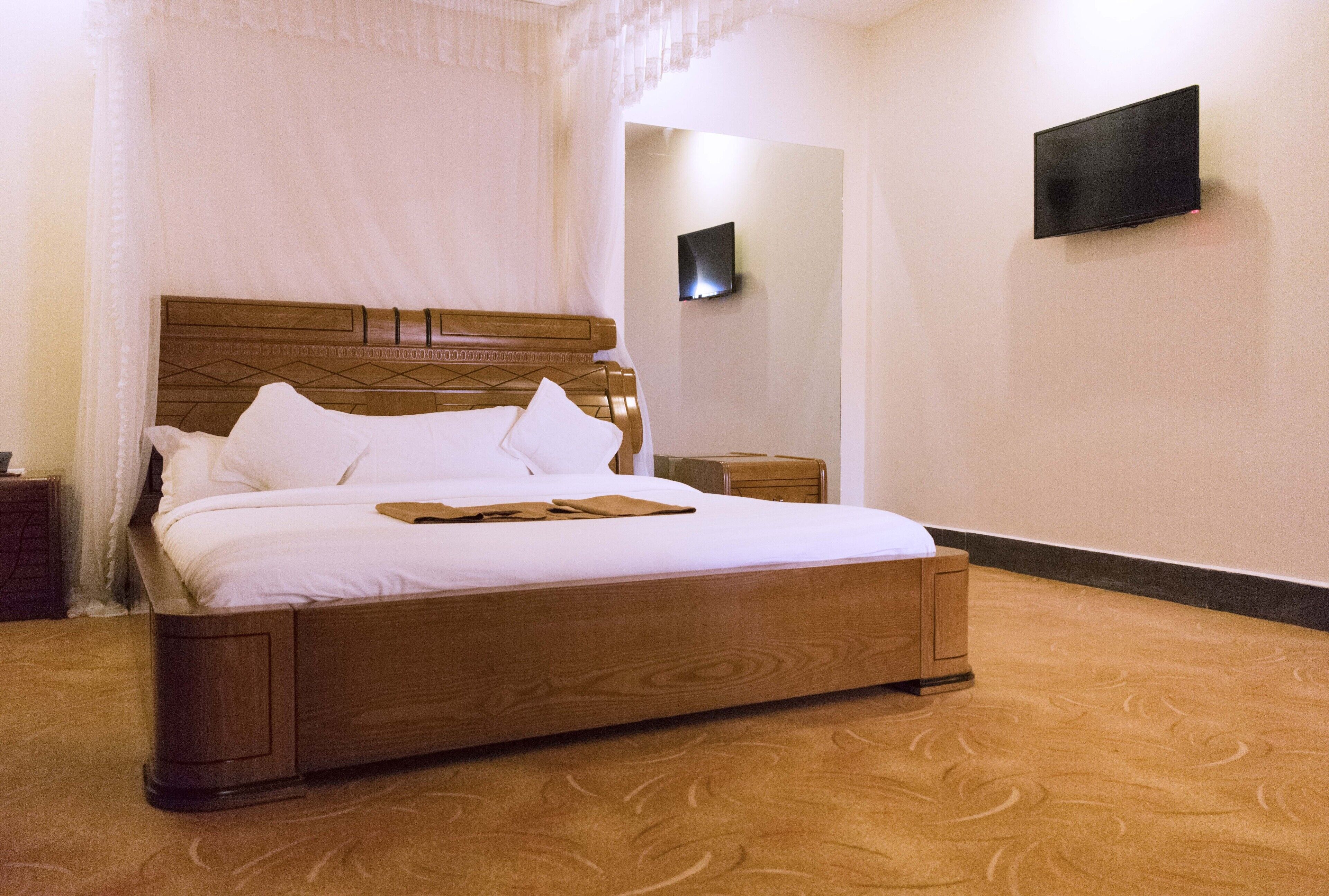 Ein ordentlich bezogenes Bett mit Holz-Kopfteil, einem Nachttisch und einem an der Wand befestigten Fernseher.