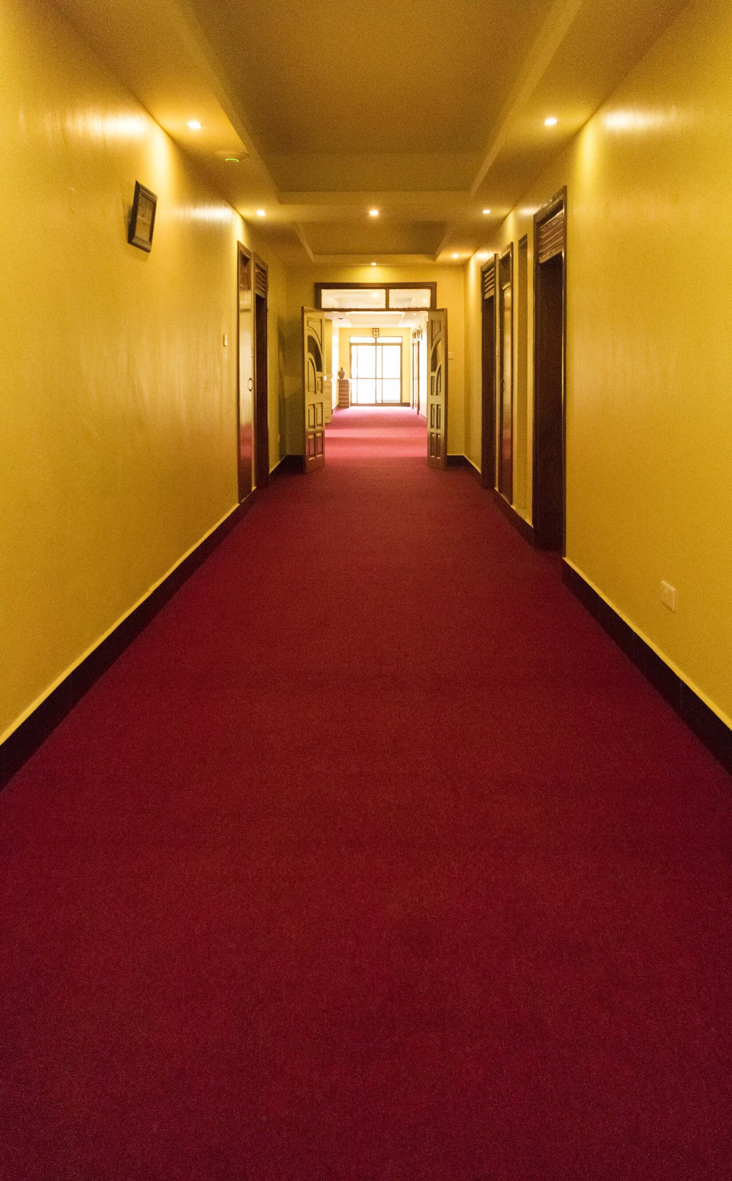 Ein Hotelkorridor mit rotem Teppich, gelben Wänden und Türen an beiden Seiten.