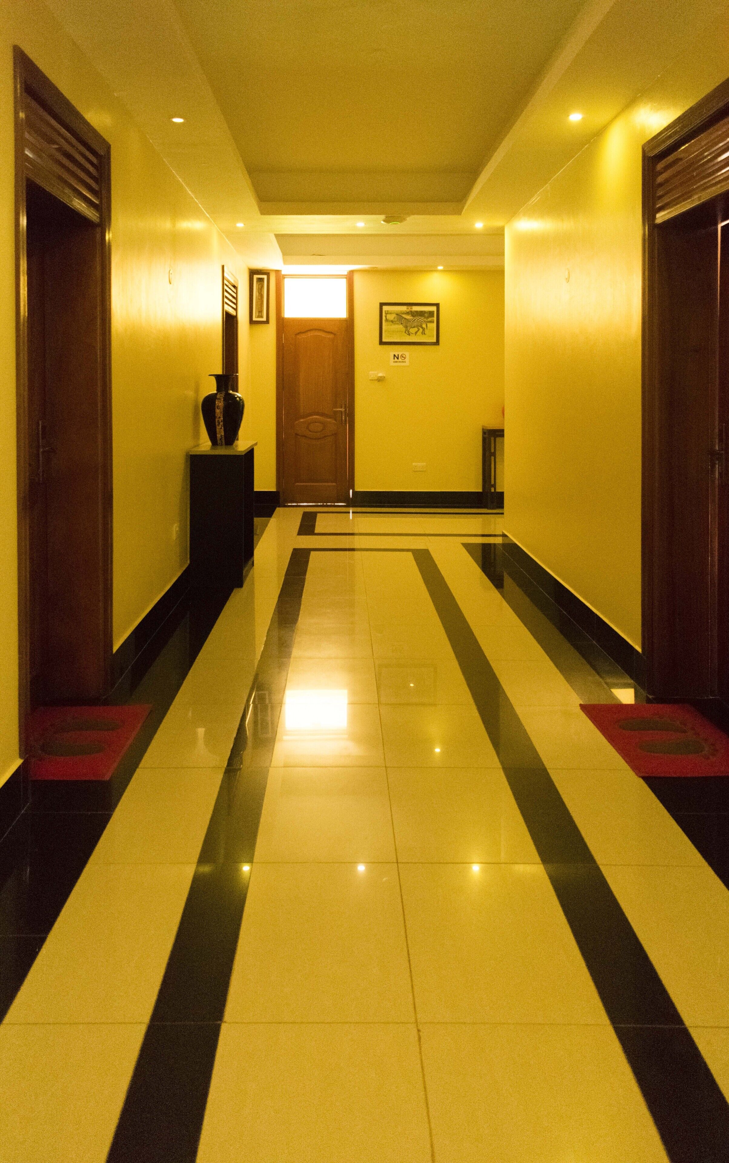 Un couloir d’hôtel avec un sol carrelé brillant, des portes en bois et un tableau encadré accroché au mur.