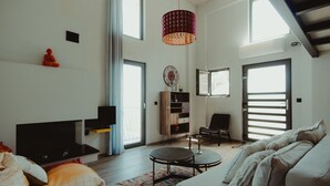 A modern living room with a sofa, a coffee table, and a TV. There is a bookshelf, a chair, and a large window. - The Z Point (Parga)