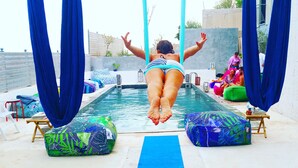 A person performing aerial yoga in a pool area with blue mats and cushions. - The Z Point (Parga)