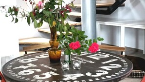 A round table with a vintage clock face, surrounded by wooden benches and a vase with flowers. - The Z Point (Parga)