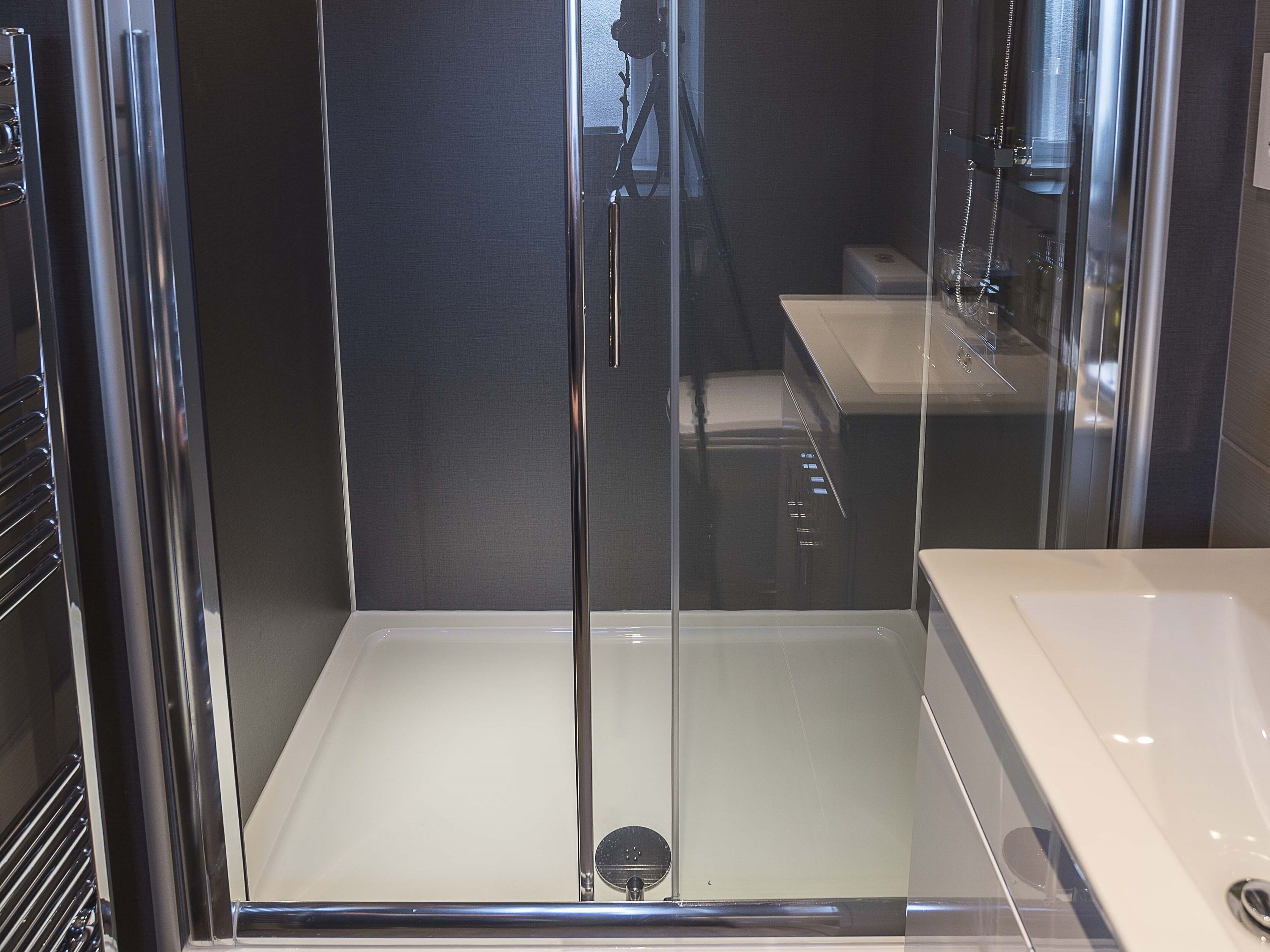 A modern bathroom with a glass-enclosed shower, a white sink, and a dark wall.