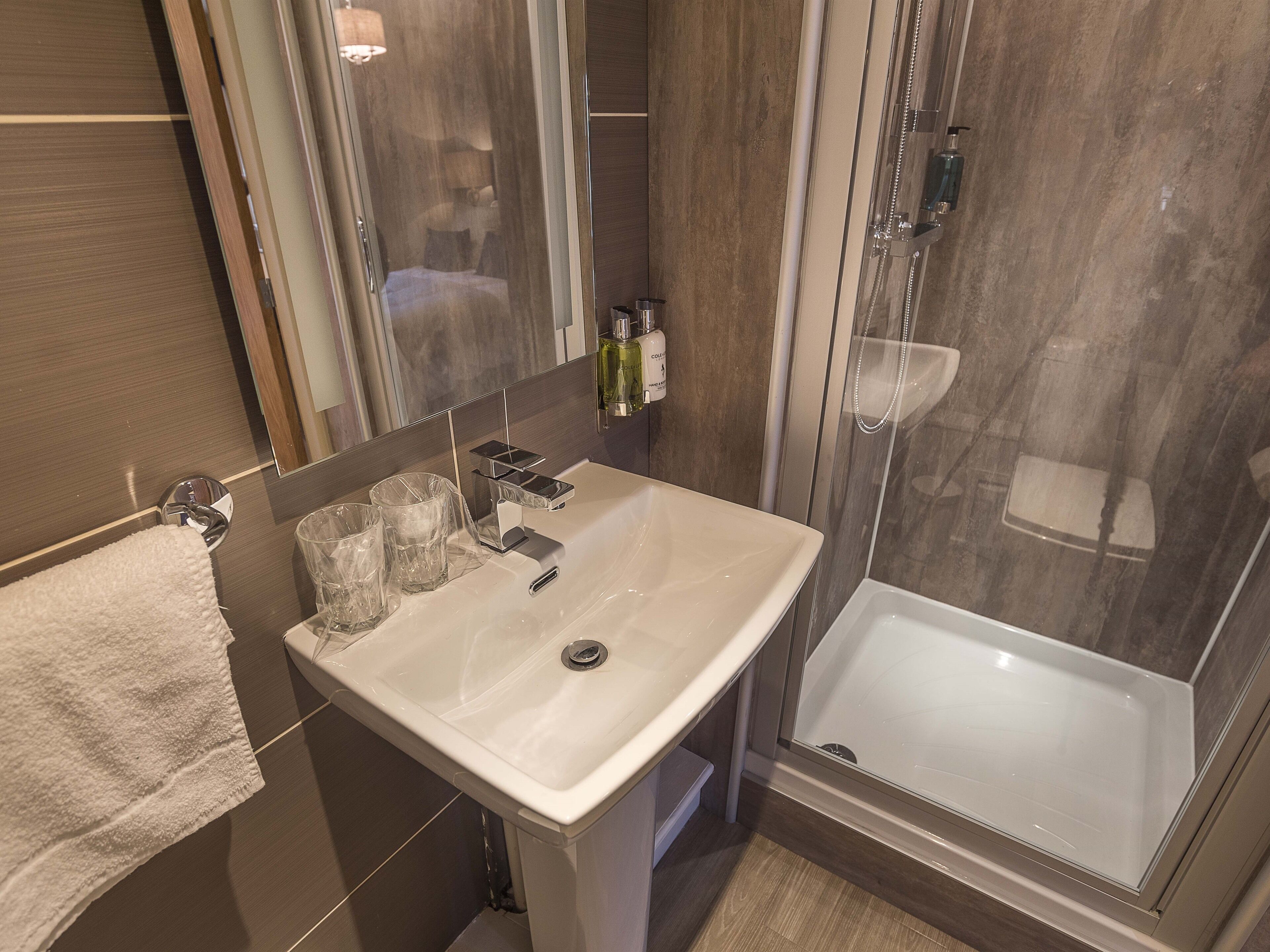 A modern bathroom with a white sink, a glass shower enclosure, and a towel on the wall.