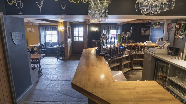 A bar area with a wooden counter, bar stools, and a chalkboard menu.