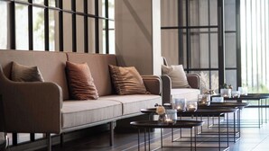 A modern lounge area with a sofa and coffee tables, large windows, and a minimalist design.