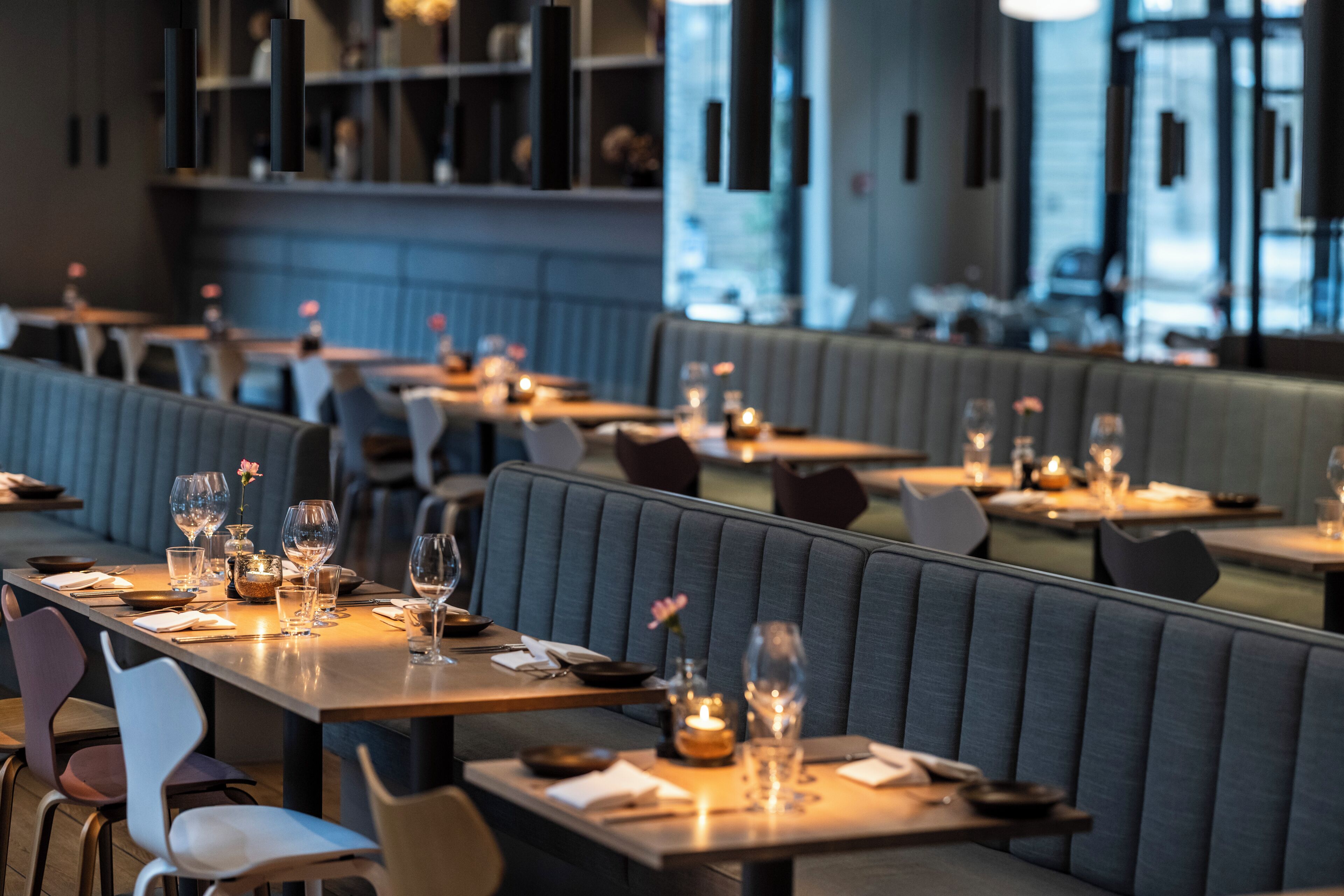 A restaurant with booths and tables, each set with glasses, cutlery, and candles.