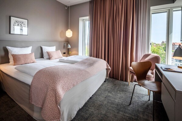 A hotel room with a large bed, a desk, a chair, a lamp, and a window with curtains.