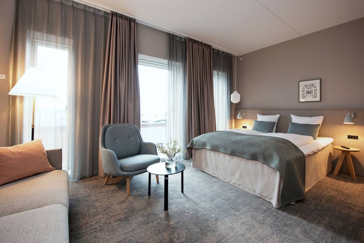 Una habitación de hotel con una cama, un sofá, una silla, una mesita y una lámpara.