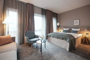 A hotel room with a bed, a sofa, a chair, a small table, and a lamp.