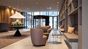 A modern lobby with a seating area, a round table with a lamp, and a view through large windows.