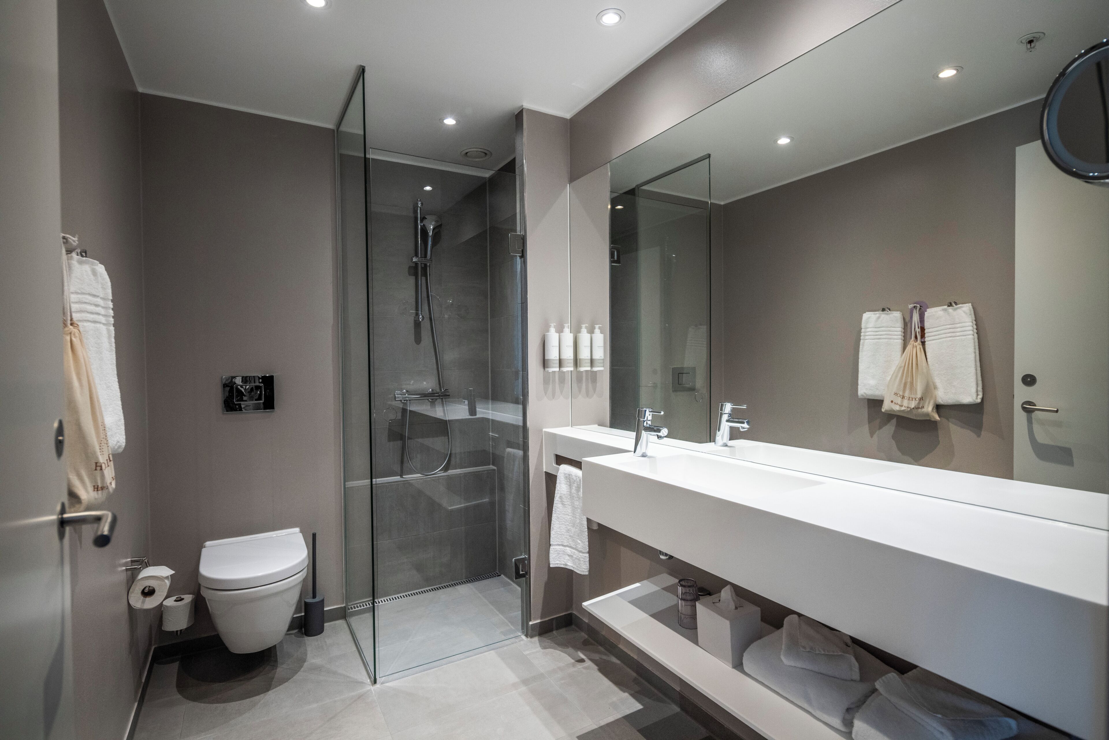 Un baño moderno con cabina de ducha de vidrio, inodoro blanco y un espejo grande sobre un lavamanos blanco.