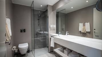 Un baño moderno con cabina de ducha de vidrio, inodoro blanco y un espejo grande sobre un lavamanos blanco.
