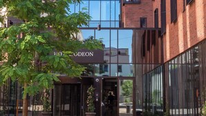 A modern building with a glass facade and a brick exterior. There is a sign for "HOTEL DEON" and a small outdoor seating area with a bench.