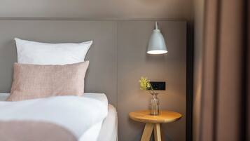 A neatly made bed with pillows, a bedside table with a vase, and a wall-mounted lamp.