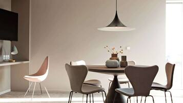 A modern dining area with a round table, four chairs, a pendant light, and a vase with flowers on the table.