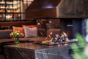 A modern fireplace with a glass enclosure, a marble countertop, and a sofa in the background.
