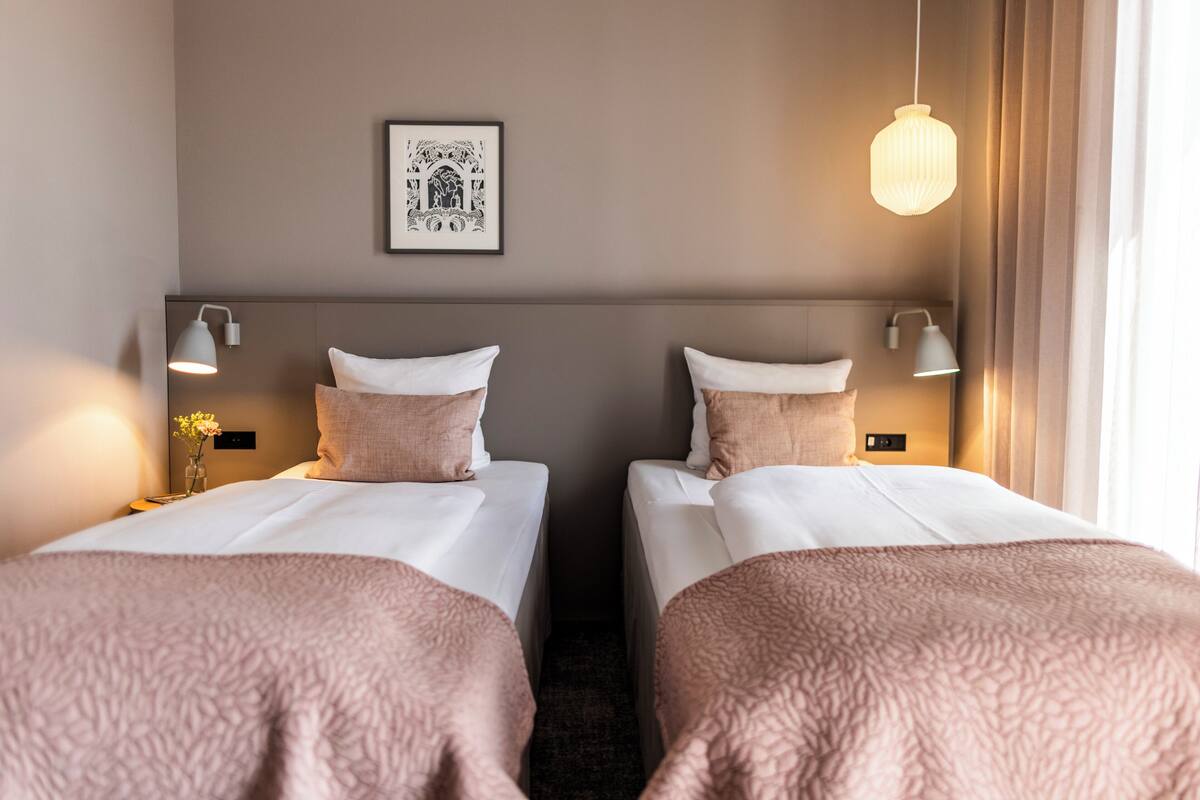 Habitación de hotel con dos camas, un cuadro en la pared y una lámpara colgante.