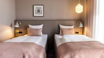 Quarto de hotel com duas camas, um quadro pendurado na parede e um candeeiro suspenso.