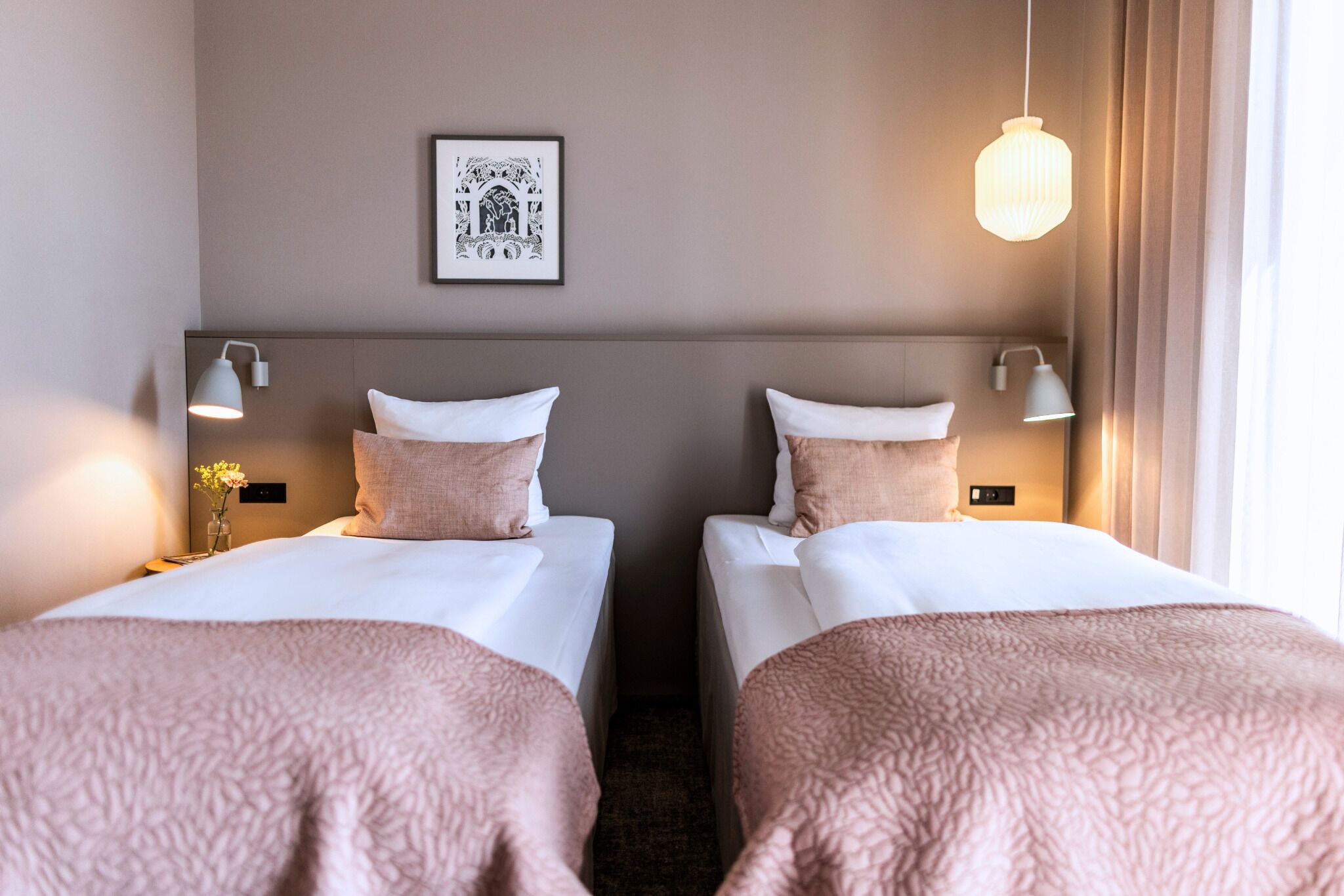 Een hotelkamer met twee bedden, een ingelijste foto aan de muur en een hanglamp.