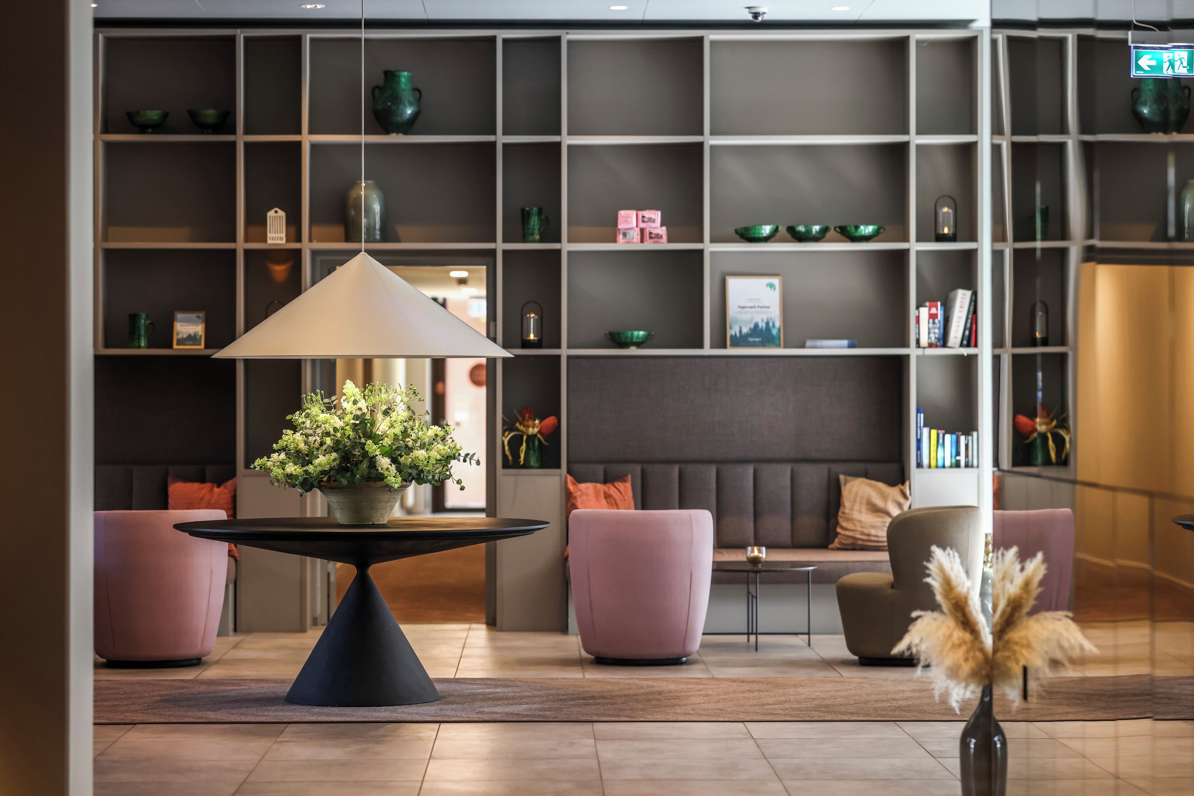 A modern lobby with a central table, seating area, and a bookshelf.