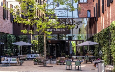 A hotel with outdoor seating, a tree, and a brick facade.