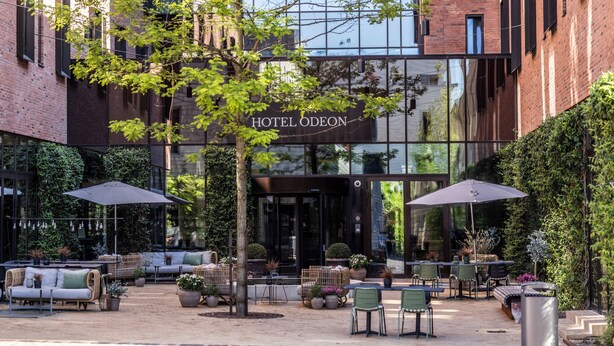 A hotel with outdoor seating, a tree, and a brick facade.