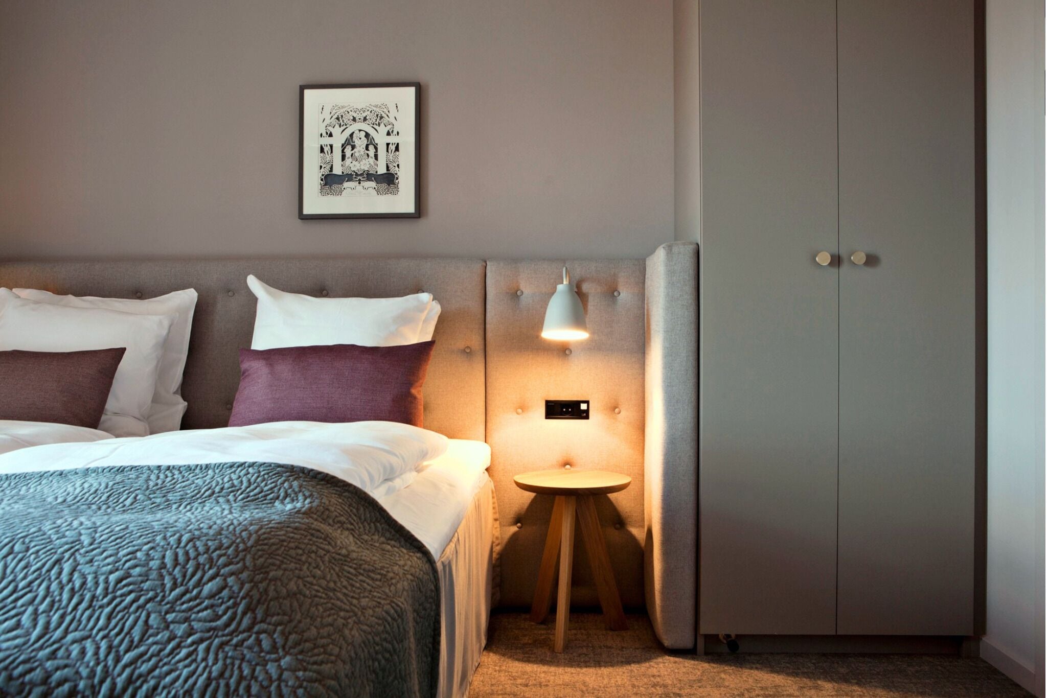 A bedroom with a bed, a bedside table with a lamp, a wardrobe, and a framed picture on the wall.