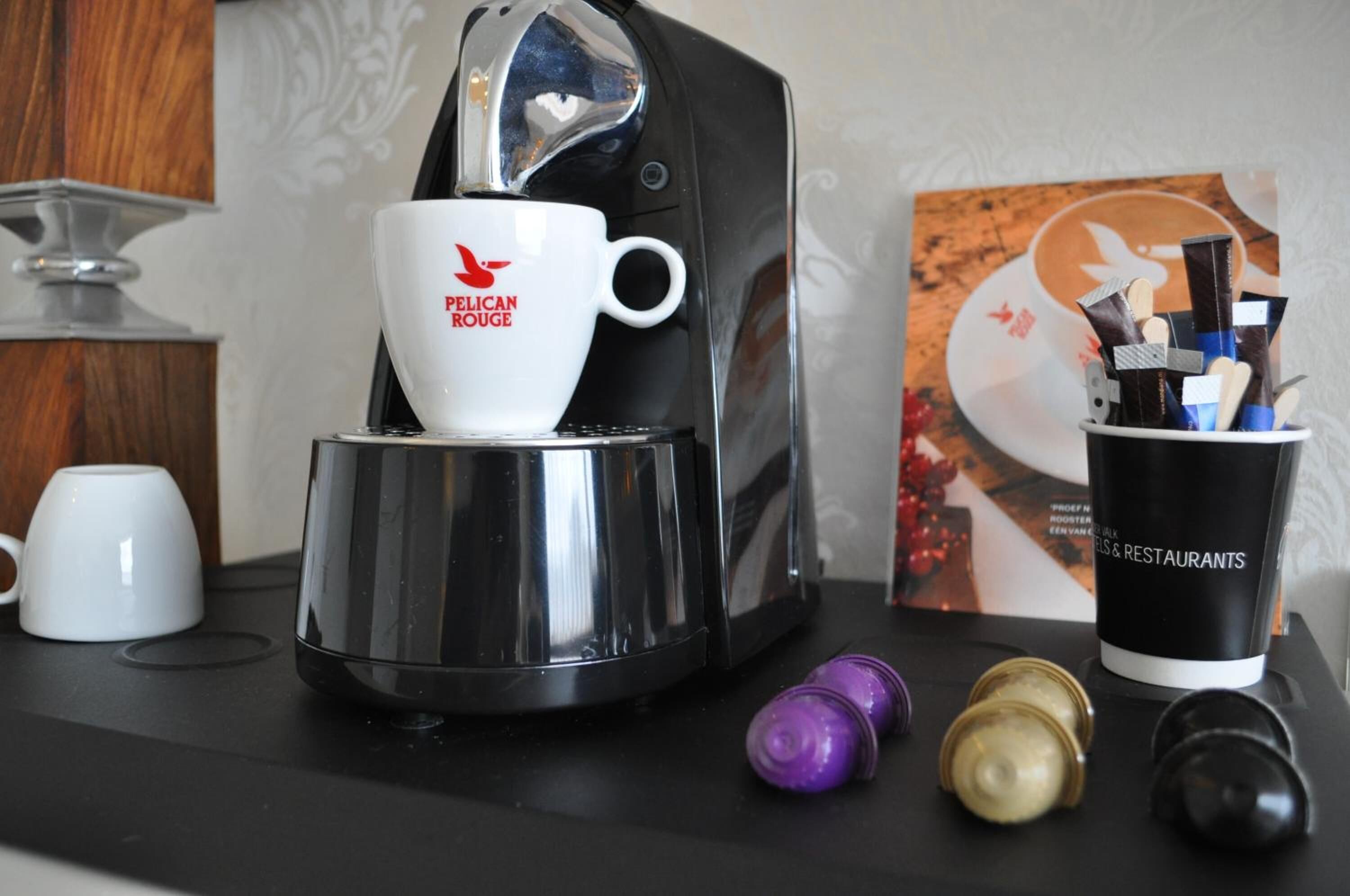 A coffee machine with a cup labeled "PELICAN ROUGE" and a coffee cup with a spoon and stirrer.