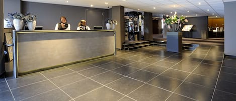 A hotel reception area with a modern design, featuring a reception desk, large decorative vases, and a spacious lobby with a tiled floor.