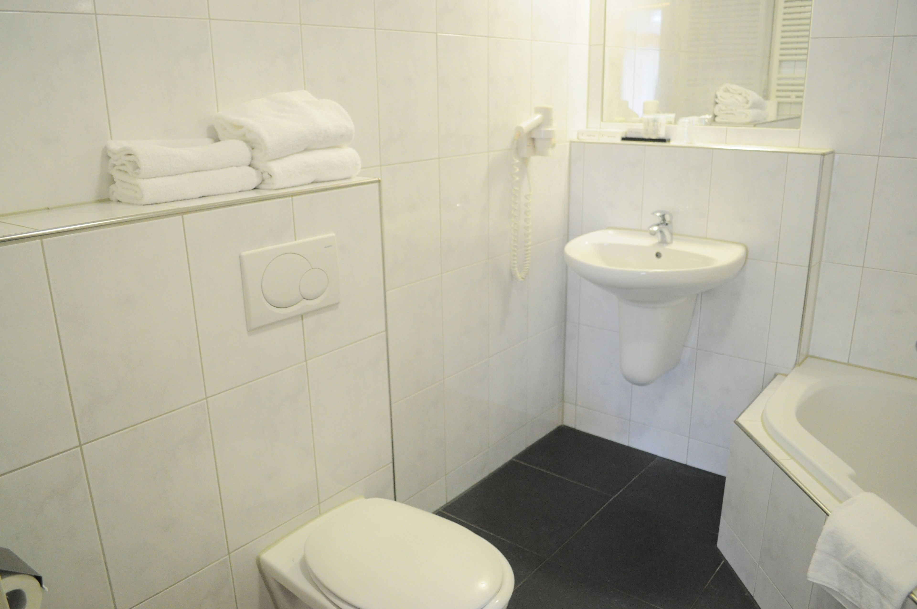 Un baño con inodoro, lavamanos y bañera. Hay toallas apiladas en un estante.