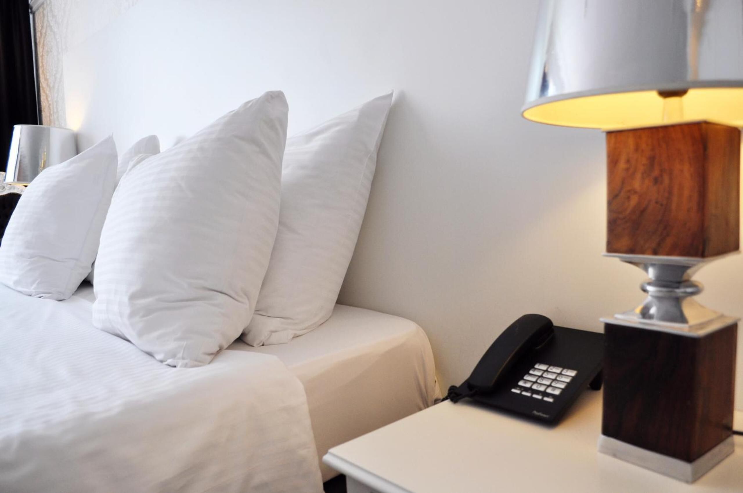 Een hotelkamer met een bed, witte kussens, een bedlampje en een telefoon.